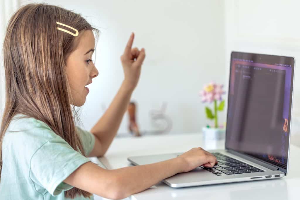 Young girl coding on a laptop with a raised finger in a bright room.