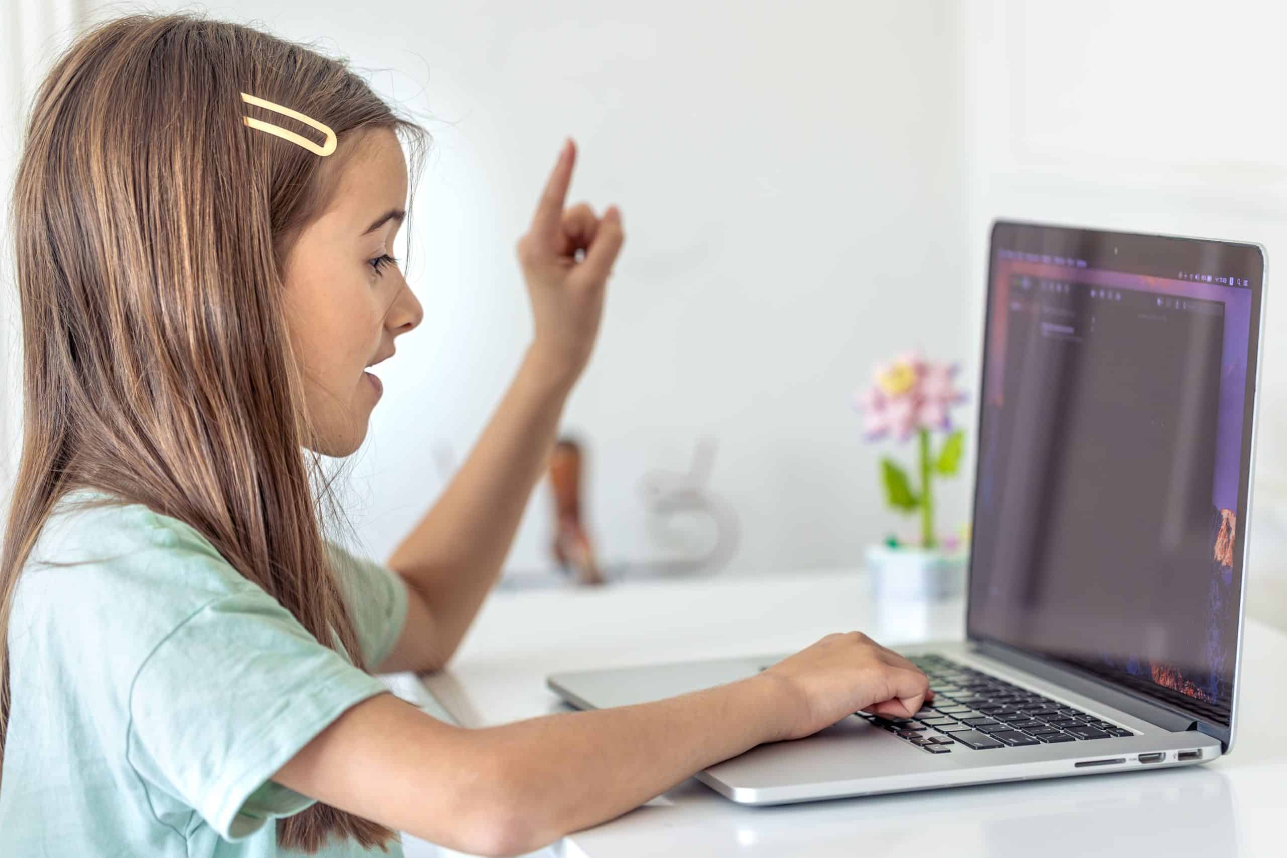 Young girl coding on a laptop with a raised finger in a bright room.