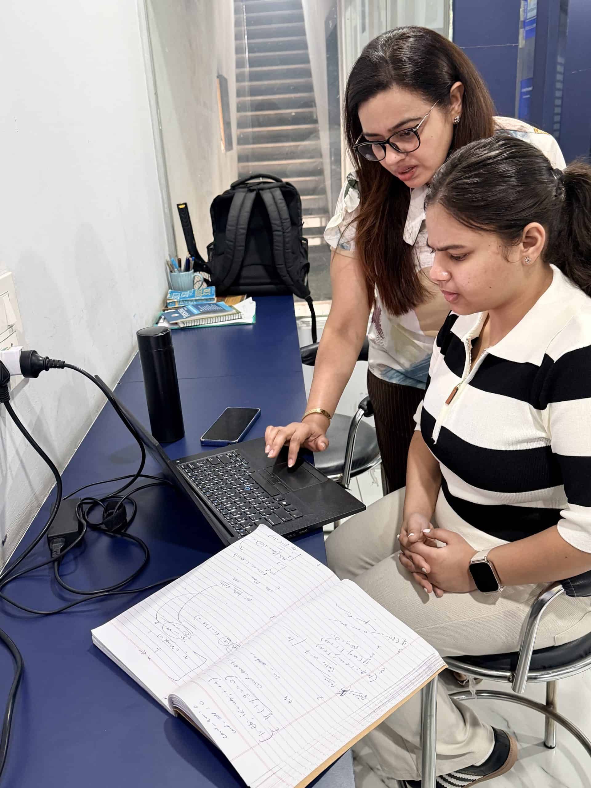 Young girl and teacher working on a laptop in a classroom setting.